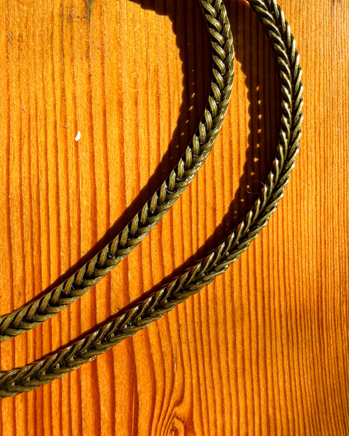 A close-up of a brass metal chain, laid diagonally across a warm orange-brown wooden surface.