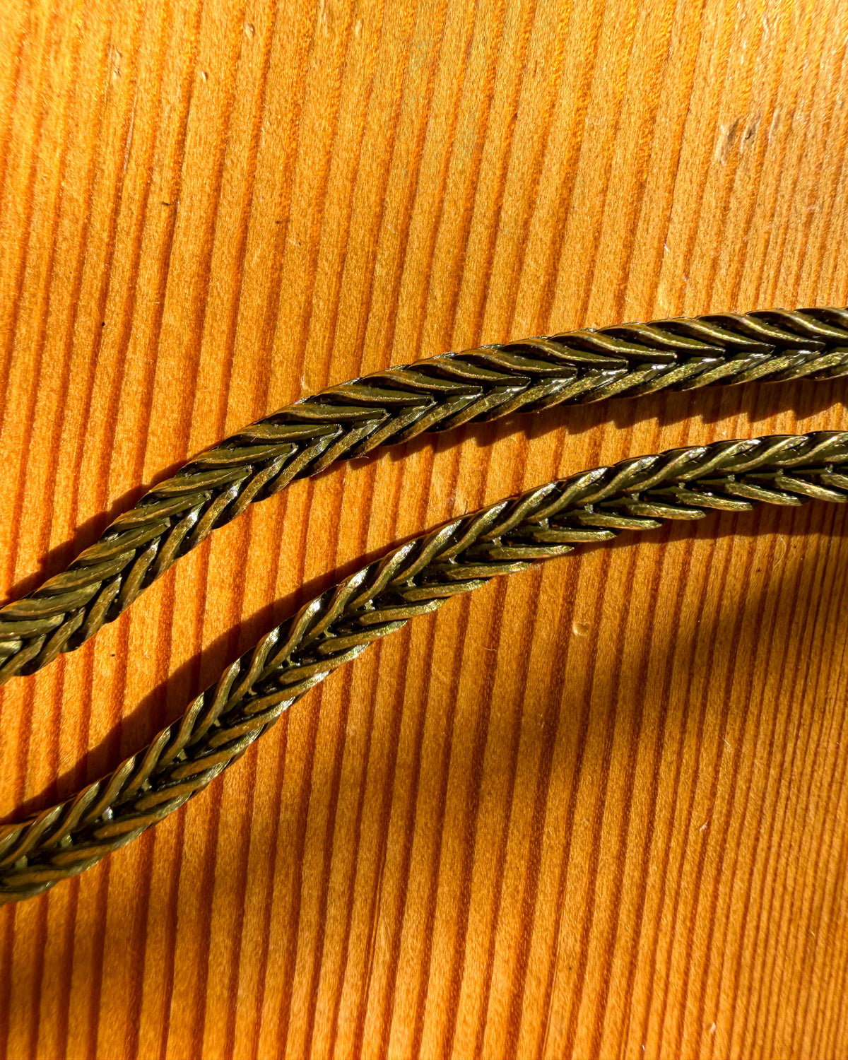 A close-up of a braided metallic chain, resting on a warm, sunlit wooden surface.
